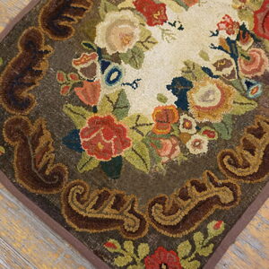Hooked rug with multicolored floral design and scrolled brown border on rustic wood flooring.