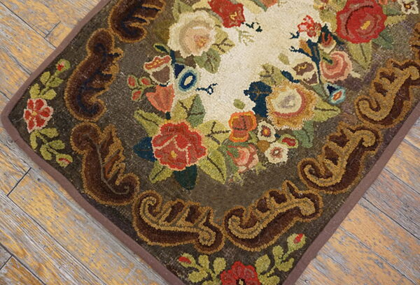 Hooked rug with multicolored floral design and scrolled brown border on rustic wood flooring.