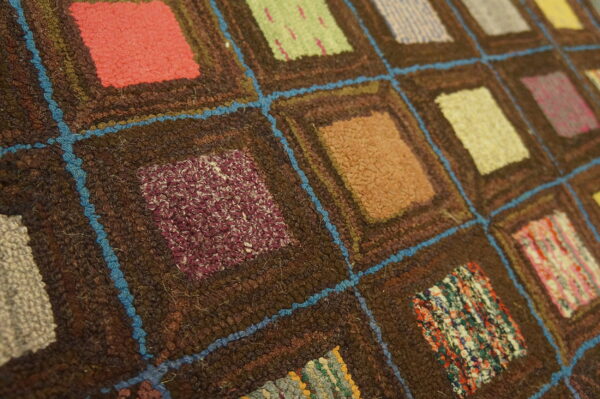 Patchwork-style rug featuring textured multicolor squares outlined in dark brown and vivid blue yarn.