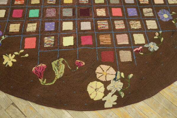 Textured brown rug with a colorful grid pattern and large floral motifs on the rounded edge set on wood flooring.