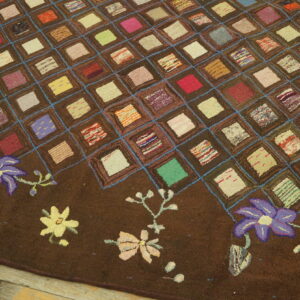 Textured brown rug with a colorful square patchwork pattern and floral border resting on wood planks.