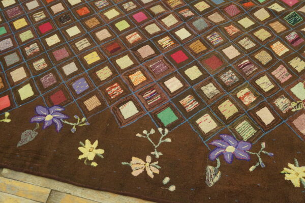 Textured brown rug with a colorful square patchwork pattern and floral border resting on wood planks.