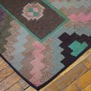 Close-up of a rustic, low-pile rug with geometric patterns in browns, pinks, greens, and purple on wood flooring.