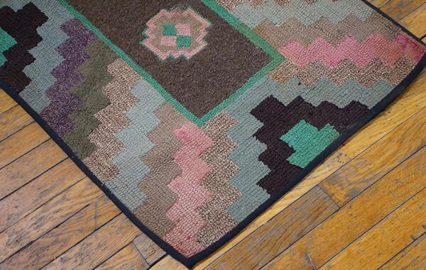 Close-up of a rustic, low-pile rug with geometric patterns in browns, pinks, greens, and purple on wood flooring.