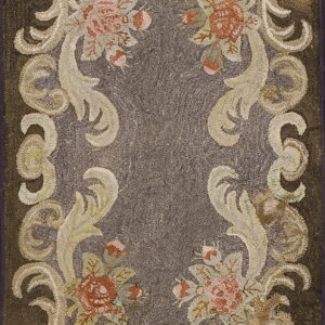 A dark brown hooked rug features a central grayish-brown field framed by ornate cream and rust floral scrollwork.