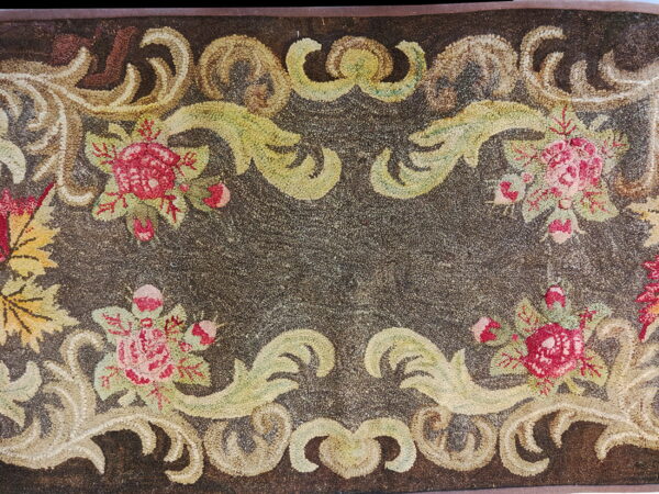 Textured dark brown rug featuring a border of pink roses and light green and beige scrolling foliage.