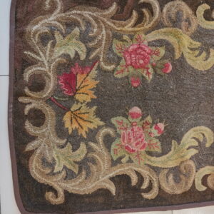 Dark brown looped rug with an ornate floral and vine pattern in pink, green, tan, and yellow tones.