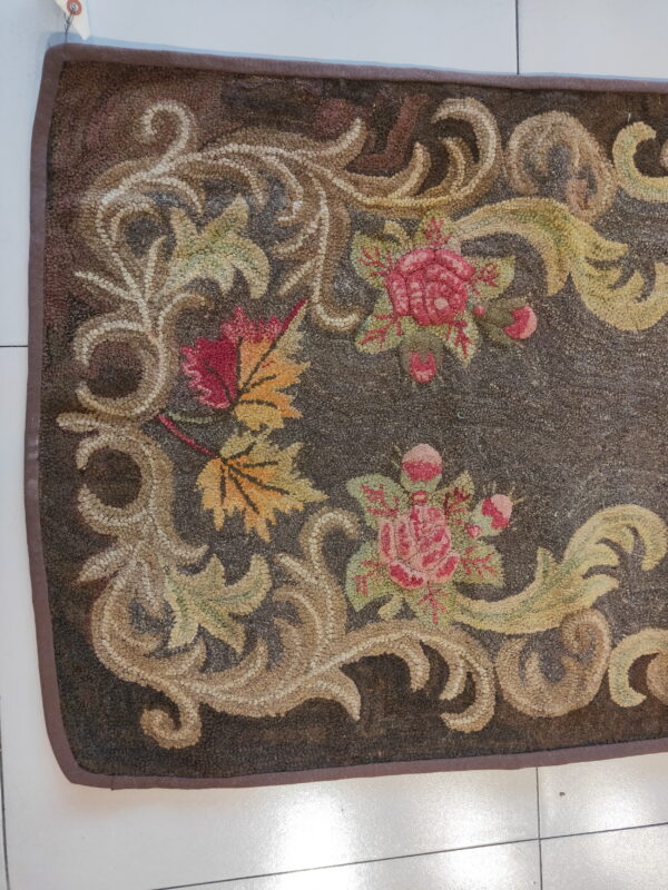 Dark brown looped rug with an ornate floral and vine pattern in pink, green, tan, and yellow tones.