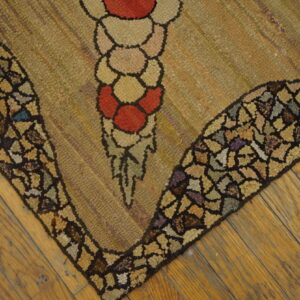 Textured rug corner featuring a red and tan floral design with a dark multicolor mosaic border on wood floors.