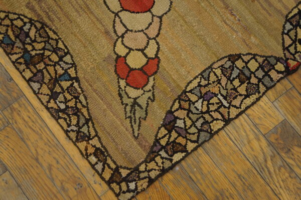 Textured rug corner featuring a red and tan floral design with a dark multicolor mosaic border on wood floors.
