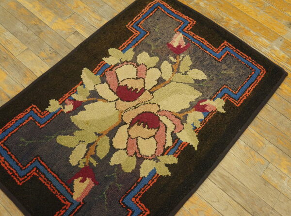 Dark, nubbly texture rug featuring a large floral design and bright geometric borders on light wood planks.
