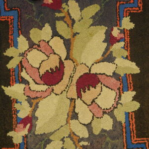 Dark, textured rug with pink and red floral motifs, green leaves, and jagged blue and orange borders.