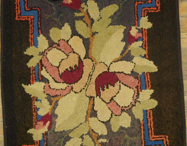 Dark, textured rug with pink and red floral motifs, green leaves, and jagged blue and orange borders.