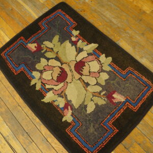 Dark brown textured rug with pink and green floral motif and geometric blue-orange borders on wood floor.