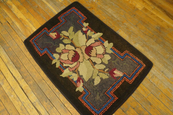 Dark brown textured rug with pink and green floral motif and geometric blue-orange borders on wood floor.