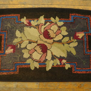 A dark hooked floral rug featuring pale flowers and a blue and orange geometric border rests on wood planks.