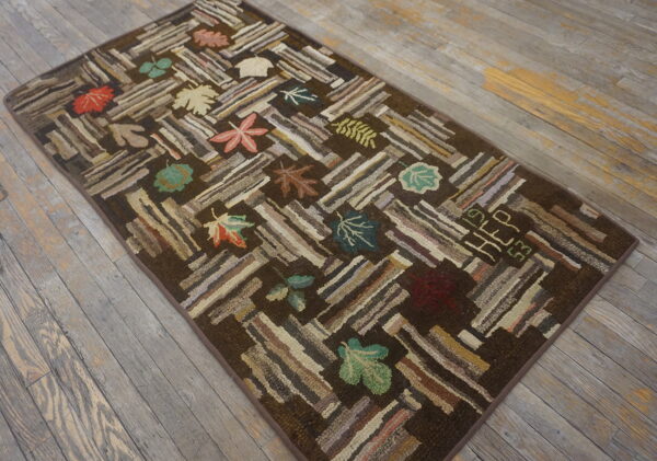 Rustic dark brown rug with a textured stripe and multicolored leaf pattern on gray wood flooring.