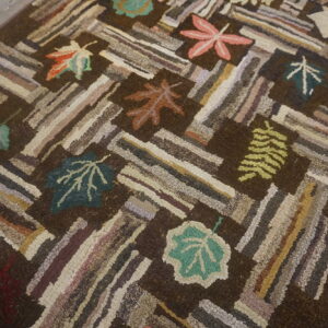 Highly textured dark brown rug featuring multicolored log cabin stripes and scattered autumn leaves on wood flooring.