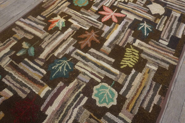 Highly textured dark brown rug featuring multicolored log cabin stripes and scattered autumn leaves on wood flooring.