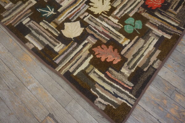 Textured brown rug with multicolored geometric log cabin strips and autumn leaf accents rests on weathered wood floors.