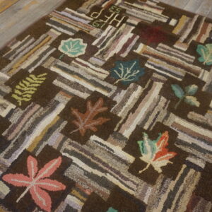 Dark brown hooked rug with multicolored striped blocks and fall leaf motifs rests on distressed wood planks.