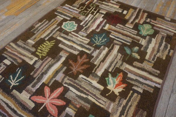 Dark brown hooked rug with multicolored striped blocks and fall leaf motifs rests on distressed wood planks.