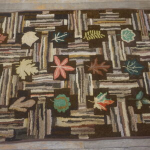 Rustic hooked rug displaying a log cabin pattern and colorful fall leaves resting on a wood floor.