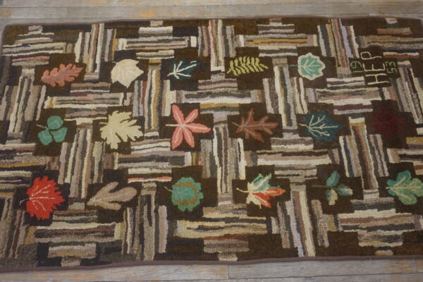 Rustic hooked rug displaying a log cabin pattern and colorful fall leaves resting on a wood floor.