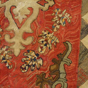 Textured rug with red field, beige stylized designs, multicolored leaves, and a geometric triangle border.