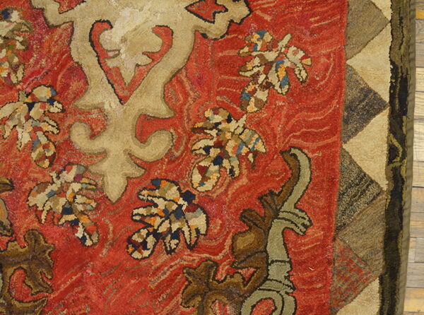 Textured rug with red field, beige stylized designs, multicolored leaves, and a geometric triangle border.