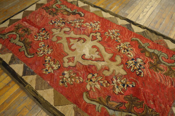 Rough texture red rug with tan scrollwork and a triangular patched border on worn wooden floorboards.