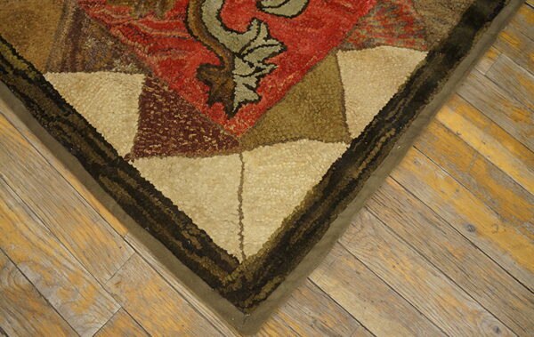 Textured, looped rug corner with red, tan, and dark geometric shapes rests on distressed wood flooring.