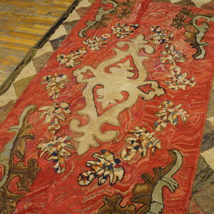 Ornate red and tan textured rug with geometric border detailing placed on rustic wooden flooring.