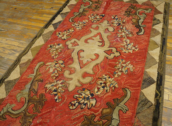 Ornate red and tan textured rug with geometric border detailing placed on rustic wooden flooring.