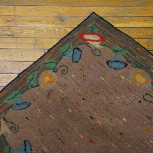Textured mauve rug with looped floral designs in green and red rests on wide plank wood flooring.