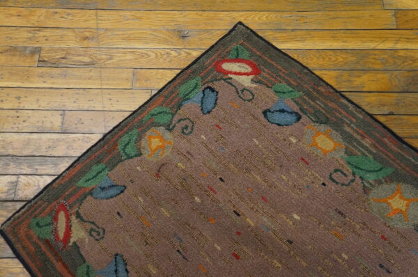 Textured mauve rug with looped floral designs in green and red rests on wide plank wood flooring.