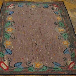 A primitive floral rug with a multicolored border framing a speckled aubergine field on distressed hardwood floors.