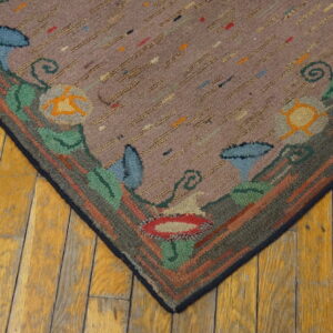 Mauve hooked rug corner with multicolored speckles, a thick floral border, and distressed yellow wood flooring.
