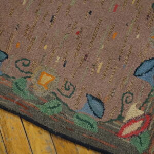 Multi-colored hooked rug featuring a dashed mauve field and thick floral border on wood floor.