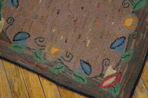 Multi-colored hooked rug featuring a dashed mauve field and thick floral border on wood floor.