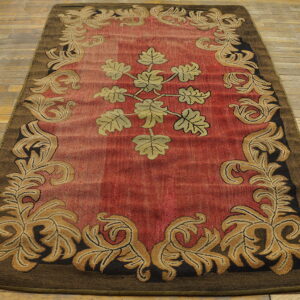 Red and gold scrolling vine rug with a dark brown border on distressed wood flooring.