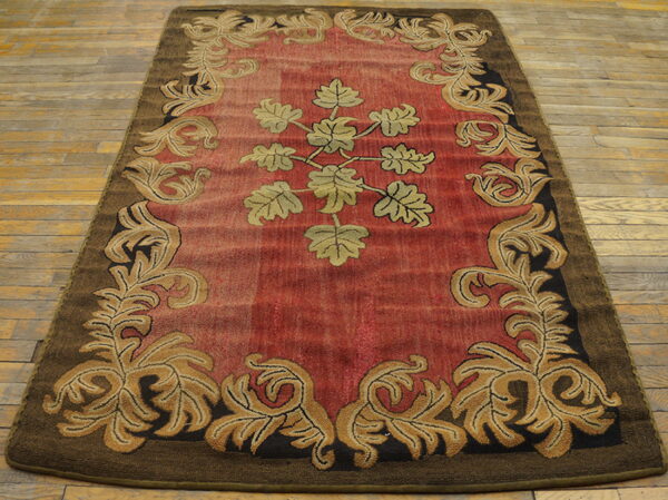 Red and gold scrolling vine rug with a dark brown border on distressed wood flooring.
