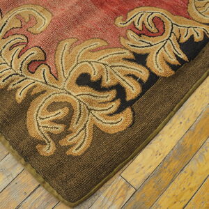 Textured rug corner features gold scrolling on a red field and a dark brown border over distressed wooden planks.