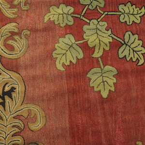 Rust-colored low-pile rug detail showing green leaves and a tan, scrolling border design.