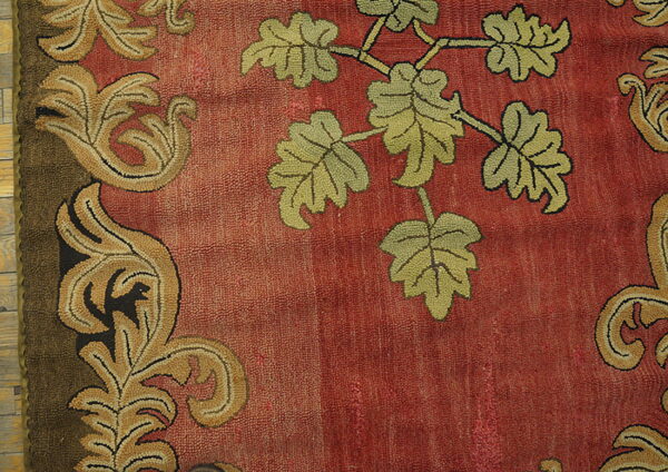 Rust-colored low-pile rug detail showing green leaves and a tan, scrolling border design.