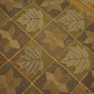 Earthy brown and green looped rug with alternating leaf and star patterns resting on chipped yellow wood planks.