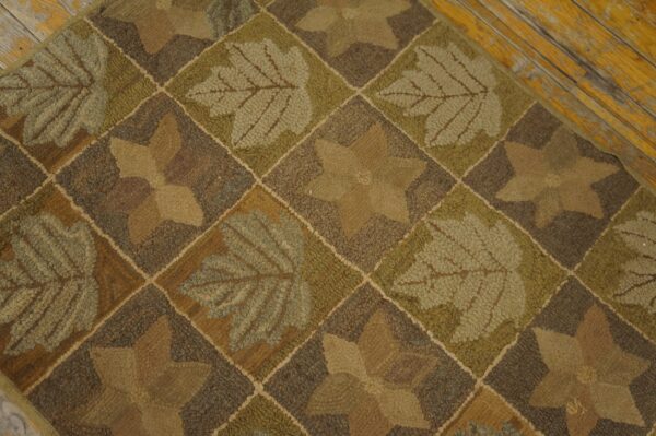 Earthy brown and green looped rug with alternating leaf and star patterns resting on chipped yellow wood planks.