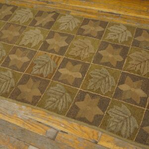 Brown and green runner with leaf and star patchwork pattern lies on worn plank wood floor.