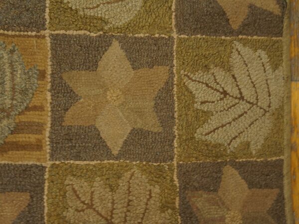 Low-pile hooked rug detail showing brown, olive green, and tan squares with leaf and star designs.