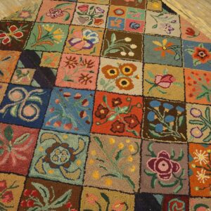 High-texture, multicolored rug with a grid of floral patterns sits diagonally on light wooden plank flooring.